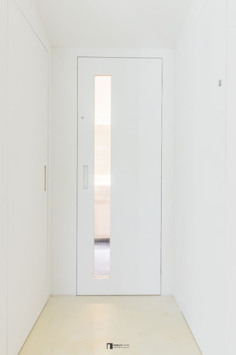 Porta battente filomuro con inserto in vetro e maniglia a incavo. Le ante sono dipinte come la parete per il massimo effetto a scomparsa