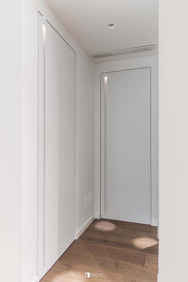 Porte battenti filomuro con maniglia a incavo tutta altezza e luce interna. Le ante sono dipinte come la parete per il massimo effetto a scomparsa